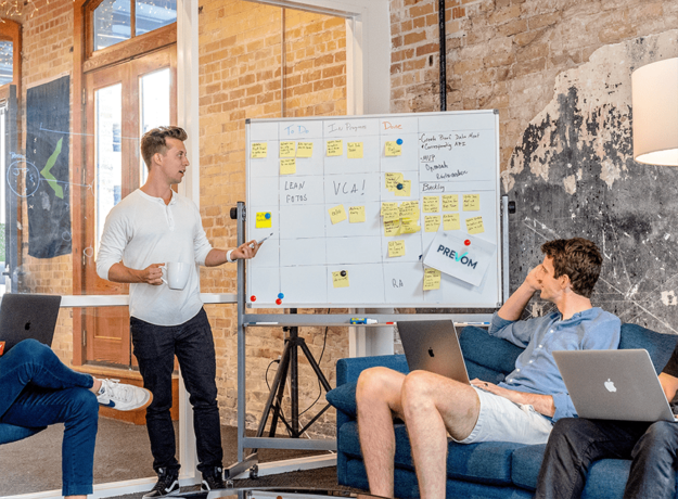 team leader next to a whiteboard talking to team members about a plan